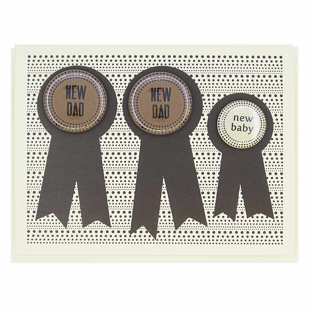 This card has three prize ribbons side by sided and features 3 buttons that can be taken off and worn by the recipients. Two say ‘New Dad’ and the other smaller button says ‘New Baby’. Perfect for the new family. Card measures 4¼” x 5½”, comes with a cream envelope & is blank inside. Designed by The Regional Assembly of Text.