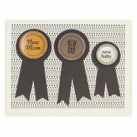 This card has three prize ribbons side by sided and features 3 buttons that can be taken off and worn by the recipients. One says ‘New Dad’, one says ‘New Mom’ and the smaller button says ‘New Baby’. Perfect for the new family. Card measures 4¼” x 5½”, comes with a cream envelope & is blank inside. Designed by The Regional Assembly of Text.