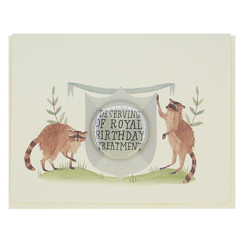 This beautiful birthday card features a watercolour painting of two raccoons on either side of a crest. There is a 1½” button in the middle of the crest which reads ‘deserving of royal birthday treatment’. The button can be taken off and worn by the recipient. Card measures 4¼” x 5½”, comes with a cream envelope & is blank inside. Designed by The Regional Assembly of Text.