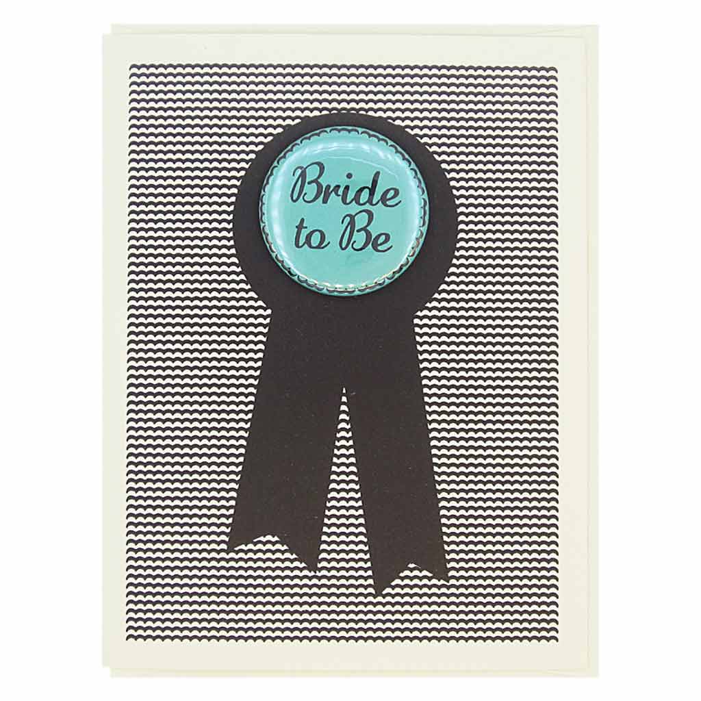 This card looks like a prize ribbon. Features a 1½” button with the text ‘Bride to Be’ that can be taken off and proudly worn by the recipient. Card measures 4¼” x 5½”, comes with a cream envelope & is blank inside. Designed by The Regional Assembly of Text.