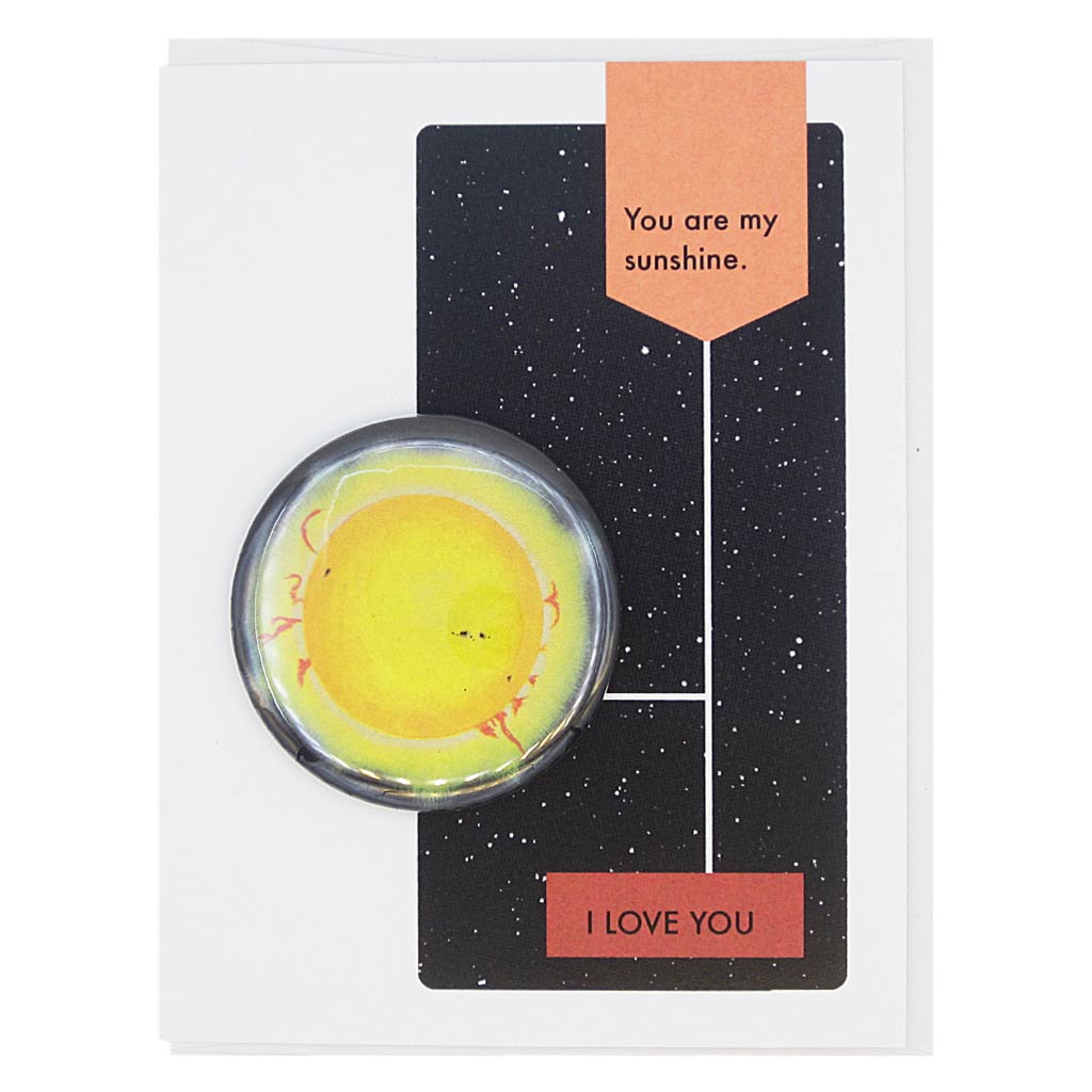This card to declare your love is designed to look like a page from a vintage science textbook with a black background of a starry sky. The text reads, ‘You are my Sunshine’ with an arrow to the text ‘I Love You’ with an arrow to a 2¼” button of a starry sky that can be taken off and worn by the recipient. Card measures 4¼” x 5½”, comes with a white envelope & is blank inside. Designed by The Regional Assembly of Text.