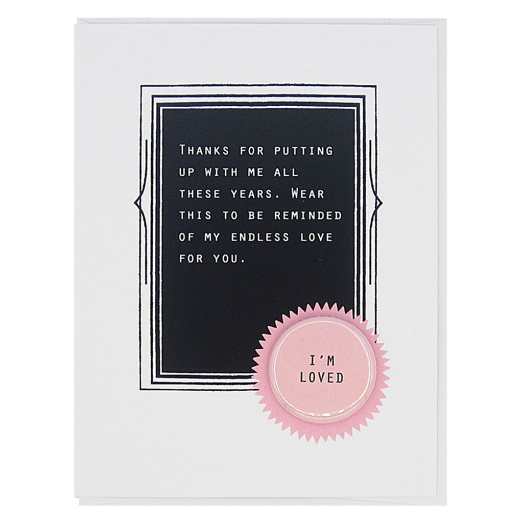 This card celebrates love. The text reads,  ‘Thanks for putting up with me all these years, wear this to be reminded of my endless love for you’. And it features a 1¼” button with the text ‘I’m Loved’ that can be taken off and proudly worn by the recipient. Card measures 4¼” x 5½”, comes with a white envelope & is blank inside. Designed by The Regional Assembly of Text.