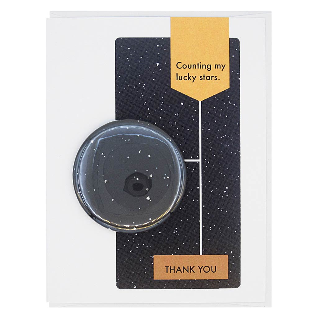 This thank you card is designed to look like a page from a vintage science textbook with a black background of a starry sky. The text reads, ‘Counting my Lucky Stars’ with an arrow to the text ‘Thank You’ with an arrow to a 2¼” button of a starry sky that can be taken off and worn by the recipient. Card measures 4¼” x 5½”, comes with a white envelope & is blank inside. Designed by The Regional Assembly of Text.