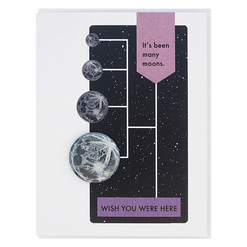 This greeting card is designed to look like a page from a vintage science textbook with a black background of a starry sky. The text reads, ‘It’s been many moons’ with an arrow to the text ‘Wish You Were Here’ with an arrow to a 1¼” button of the Moon that can be taken off and worn by the recipient. Card measures 4¼” x 5½”, comes with a white envelope & is blank inside. Designed by The Regional Assembly of Text.